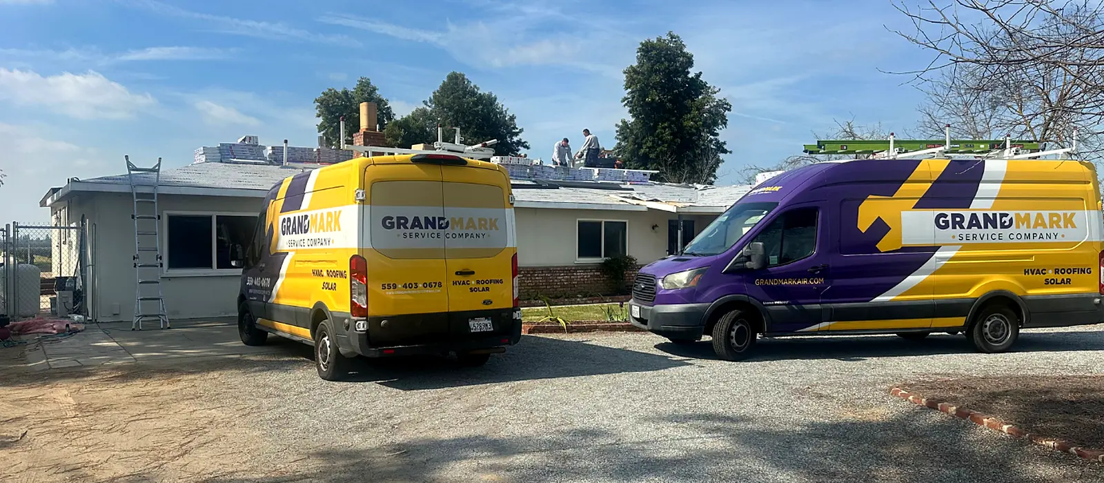 Two Grandmark vans parked at a Central Valley home while the crew works on the roof, with new material staged along the ridge
