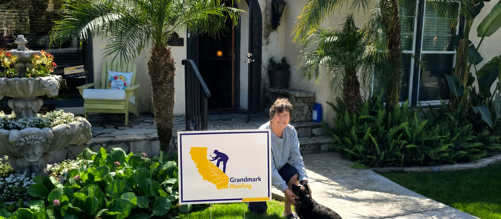 A Grandmark Roofing customer kneeling with her dog beside a Grandmark Roofing yard sign outside her home