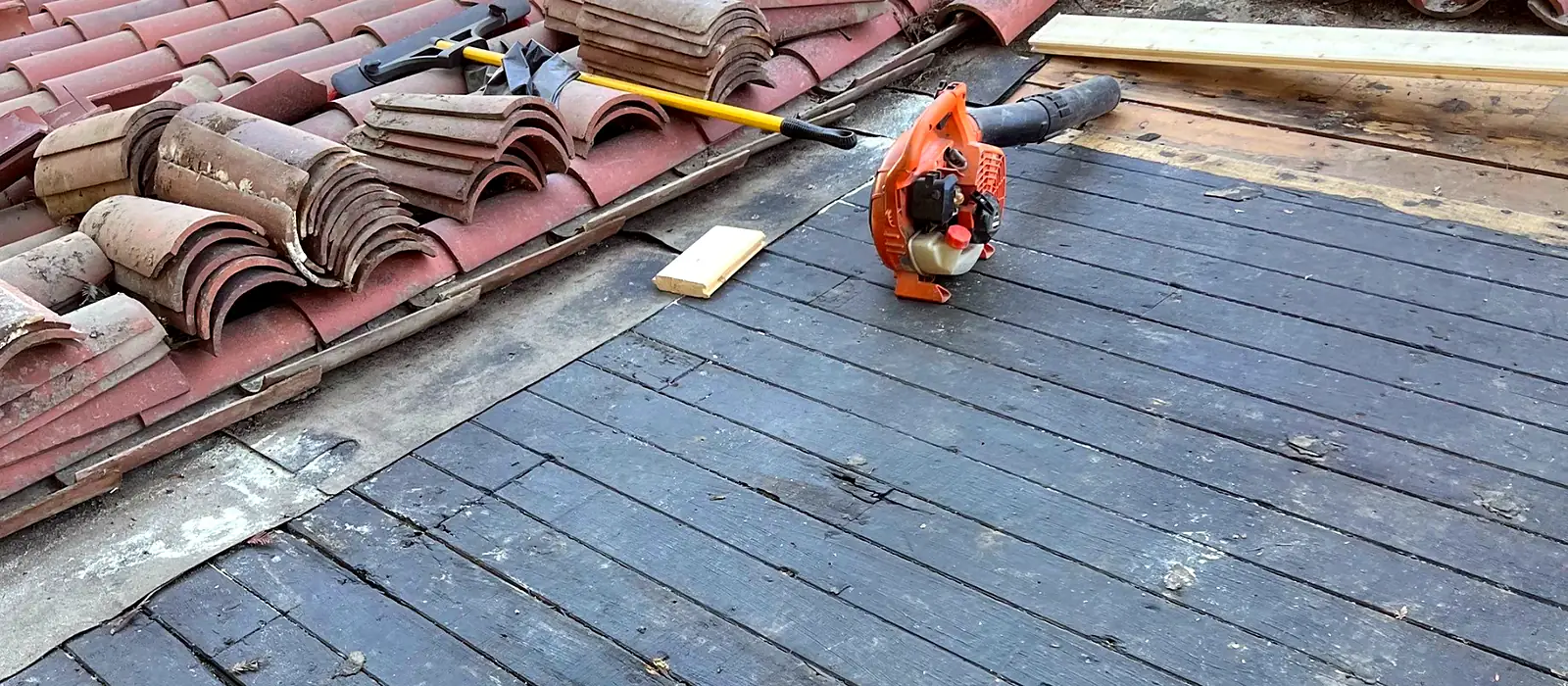 Barrel tile stacked to one side of a Fresno roof with the wood deck stripped bare and weathered underneath