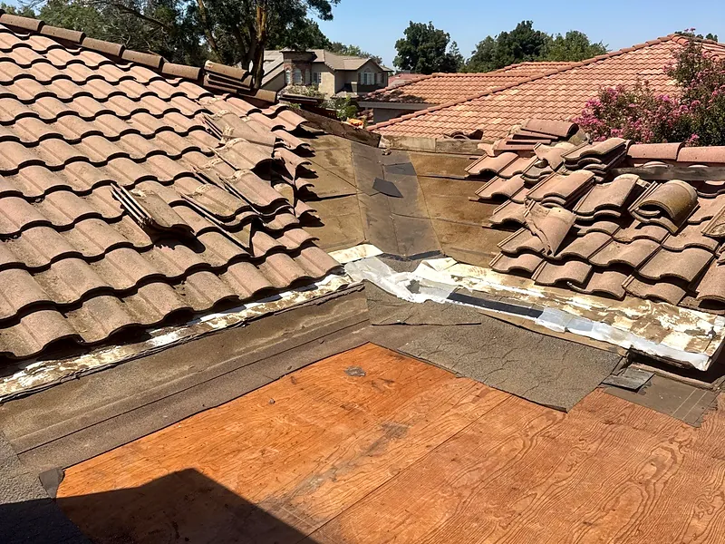 Tile stripped back on a Madera roof exposing failed underlayment and newly replaced plywood decking on the low-slope section