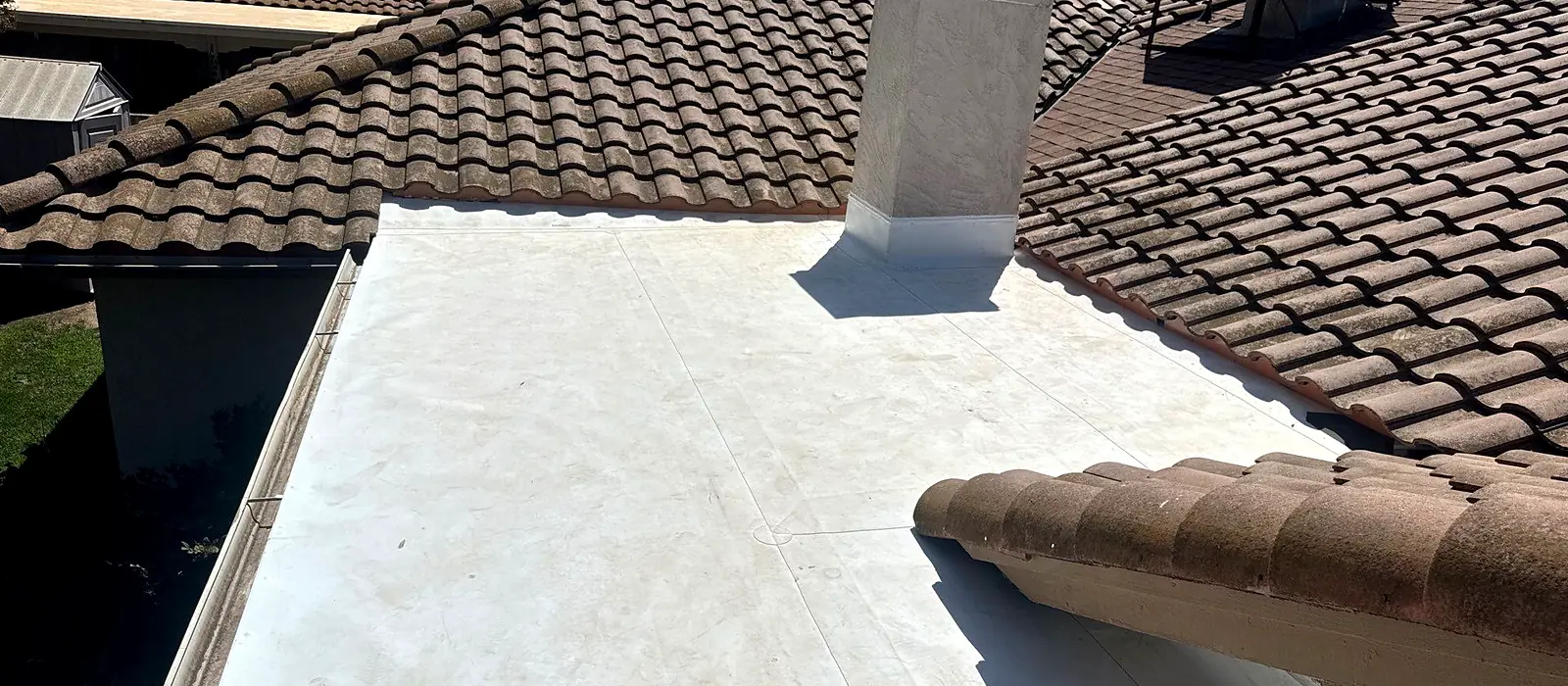 A finished white membrane roof on the low-slope section of a Madera tile home, flashed into the chimney and the surrounding tile