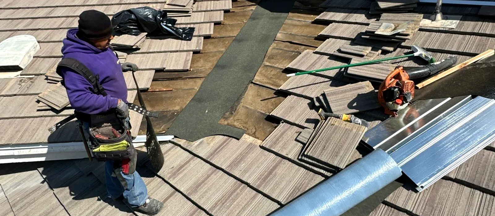 A Grandmark roofer lifting concrete tile to expose a stripped valley while tracing a leak