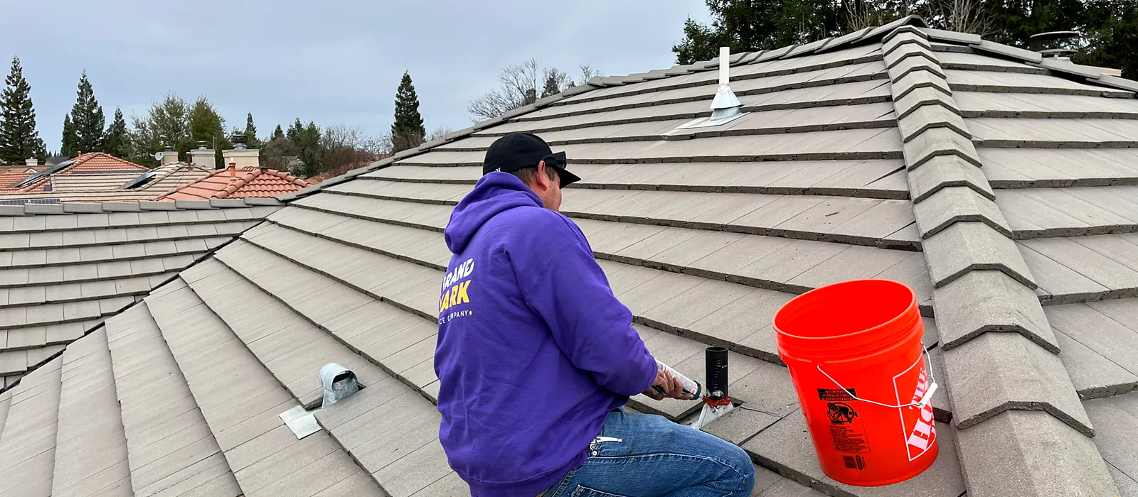 A Grandmark roofer sealing a pipe penetration and flashing on a concrete tile roof