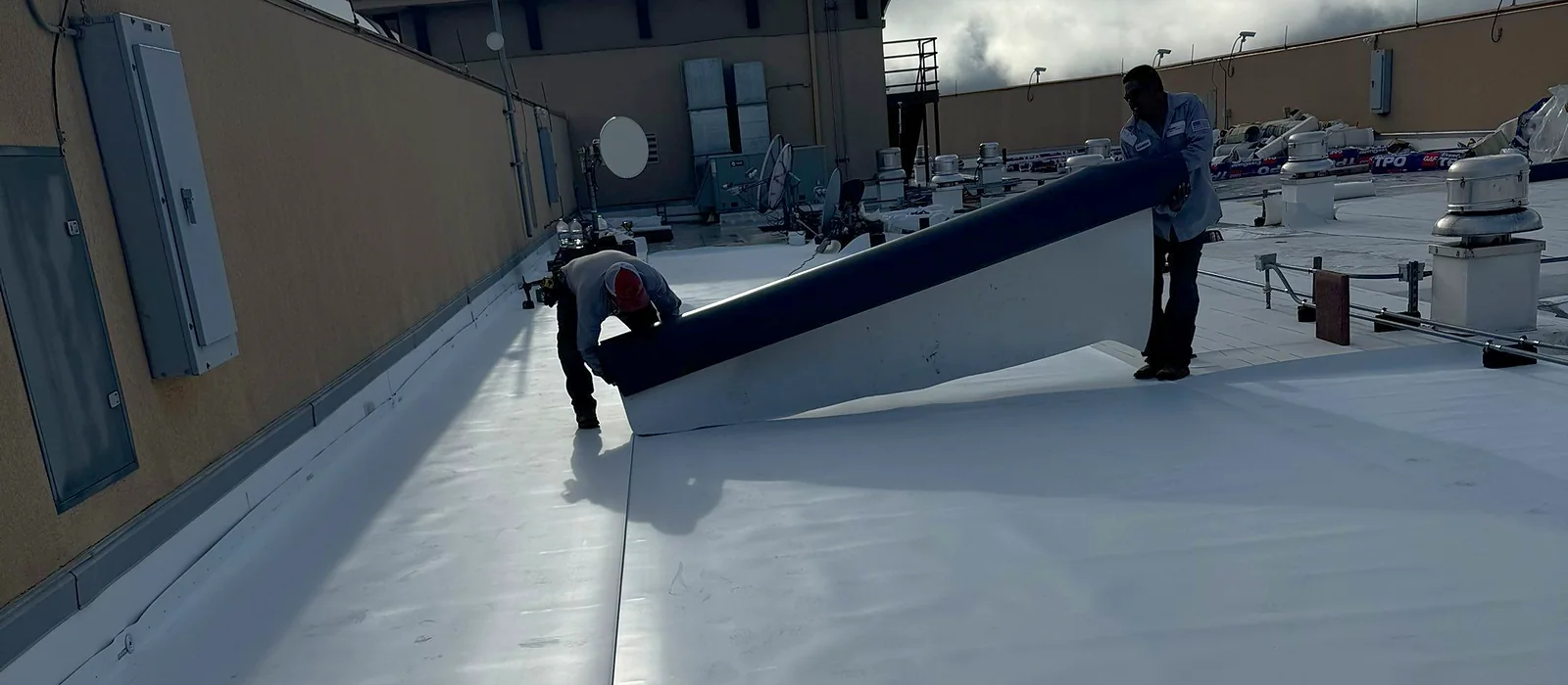 A Grandmark crew rolling out a TPO membrane sheet across a commercial flat roof