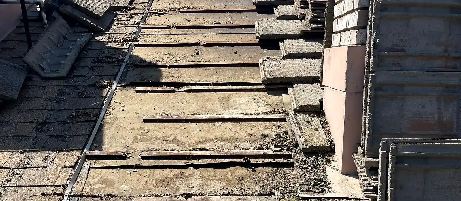 Concrete tile lifted on a Visalia roof, showing battens and packed debris beside the chimney
