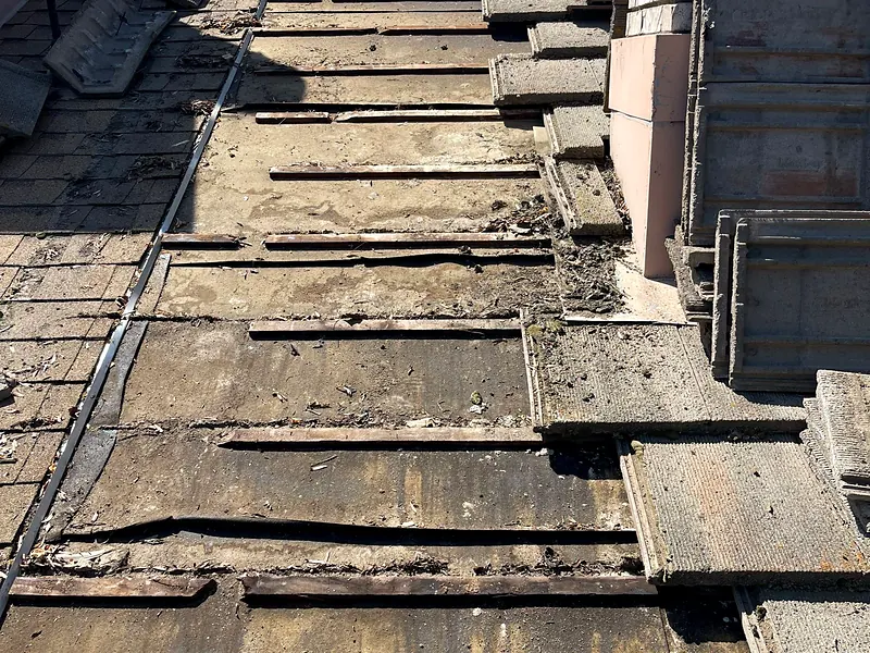 Concrete tile lifted on a Visalia roof, showing battens and debris packed along the valley