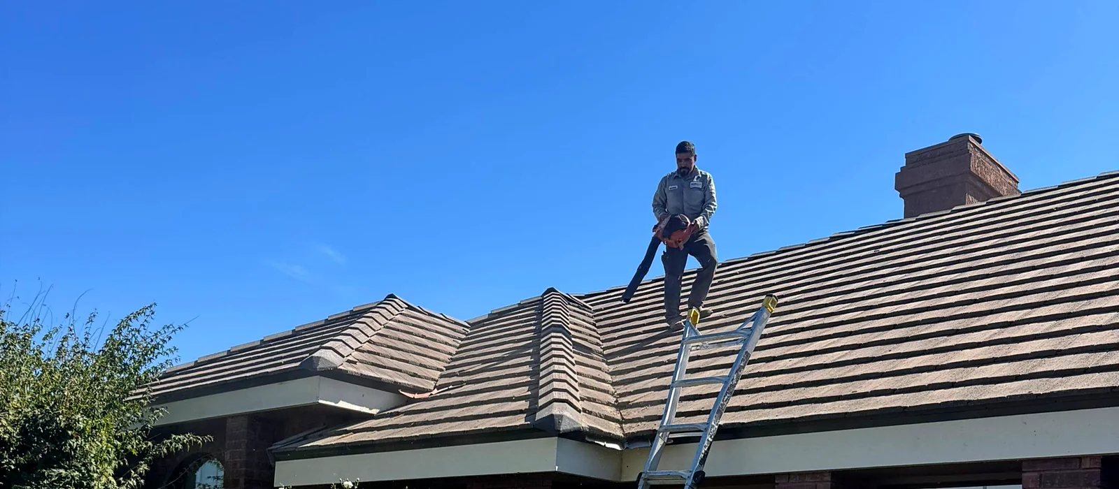 A Grandmark technician clearing debris from a concrete tile roof in Kerman during a maintenance visit