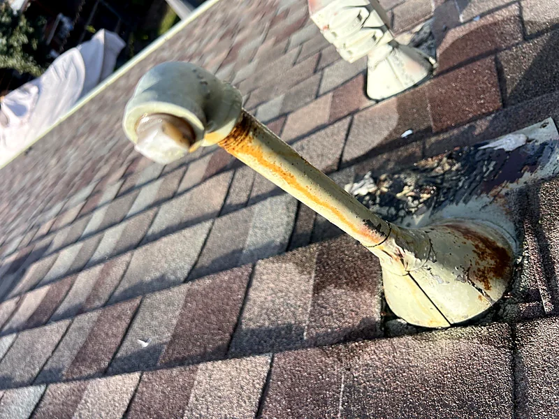 A rusted plumbing vent and failed boot on a Merced shingle roof, with sealant and debris packed around the base