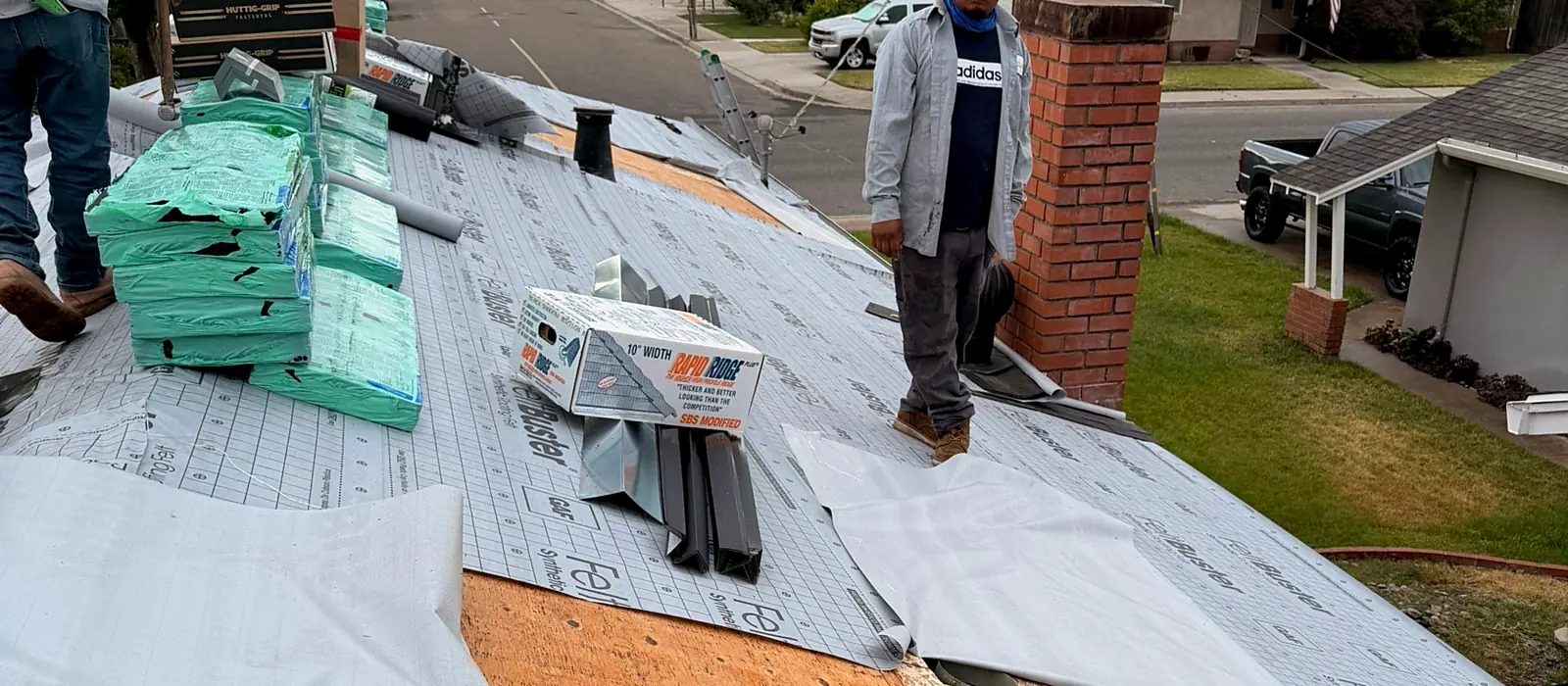 A Grandmark crew on an Oakdale roof with the repaired plywood deck exposed and synthetic underlayment going down before the new shingles