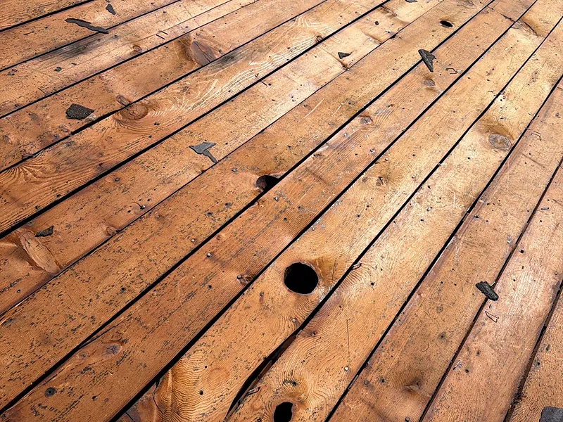 Original board sheathing exposed during a Sanger roof replacement, with wide gaps and knot holes between the boards where fasteners have nothing solid to bite into