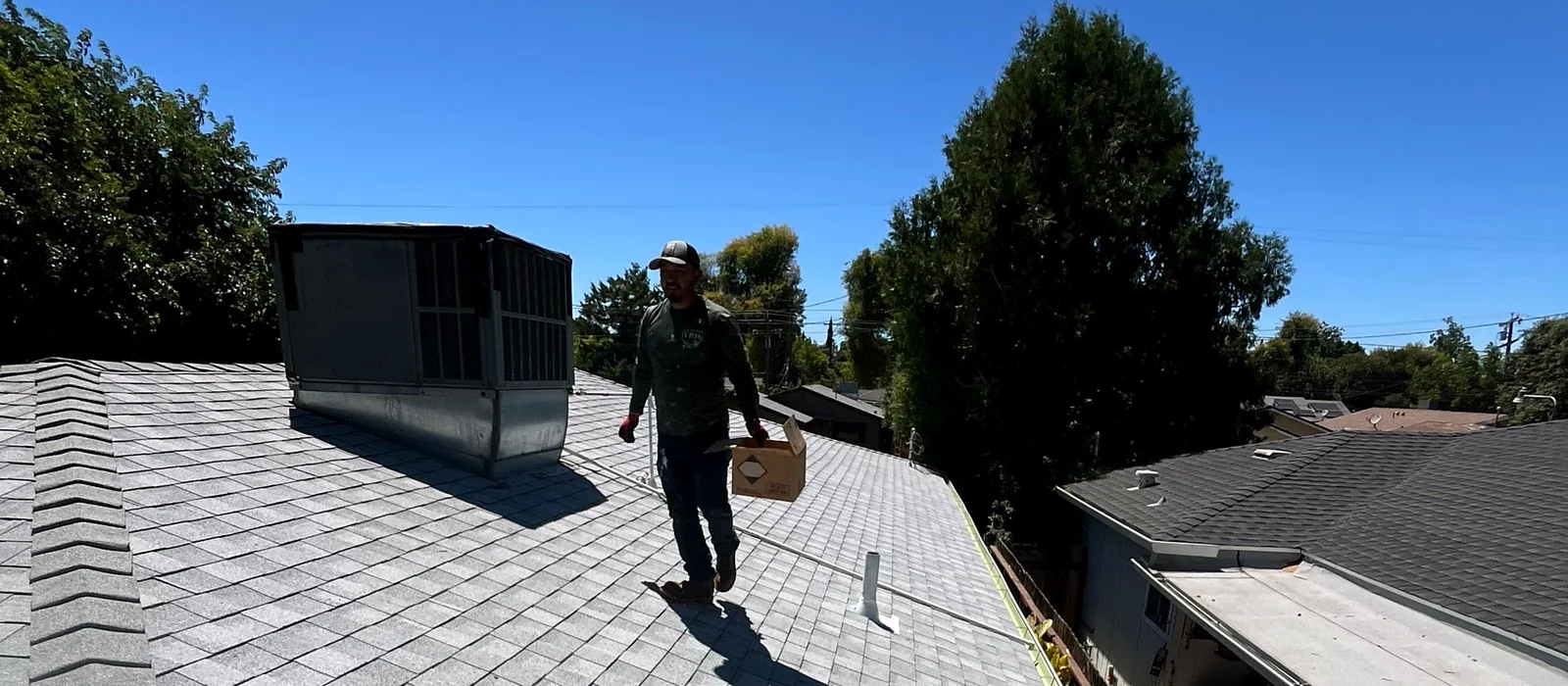 A Grandmark crew member walking a finished composition shingle roof in Stockton, with the evaporative cooler reset on the ridge and new gutter along the edge